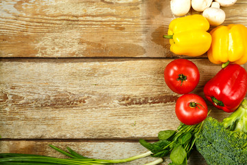 Fresh vegetables broccoli, green onions, tomatoes and peppers, mushrooms along the edge of the table from rough boards.