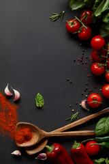 top view of cherry tomatoes, spicy chili peppers, garlic cloves and fresh herbs near spoons with paprika powder on black