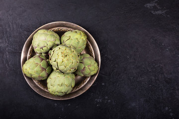 Pile of green Spanish or Italian Artichokes on the metal rustic plate, copy space