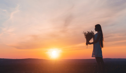 Fototapeta premium Young woman with flowers during sunset