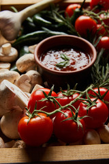 selective focus of mushrooms, cherry tomatoes, tomato sauce near rosemary and green chili peppers in wooden box