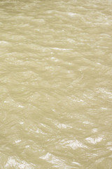 Natural texture and background. Sunlight and glare on the waves of yellow muddy tropical water