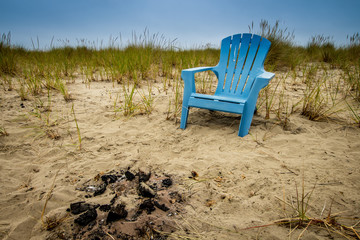 A blue lawn chair on the beach next to a camp fire