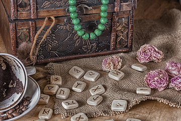 Isoteric concept of divination and prediction. Tarot cards, runes, coffee grounds in a cup, rosary, dried flower on a table against the background of an old chest.