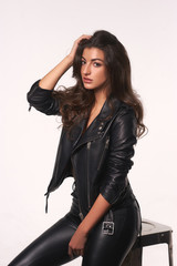 Young beautiful sexy woman with long wavy hair in black leather trousers and jacket posing against white background. Fashion style portrait