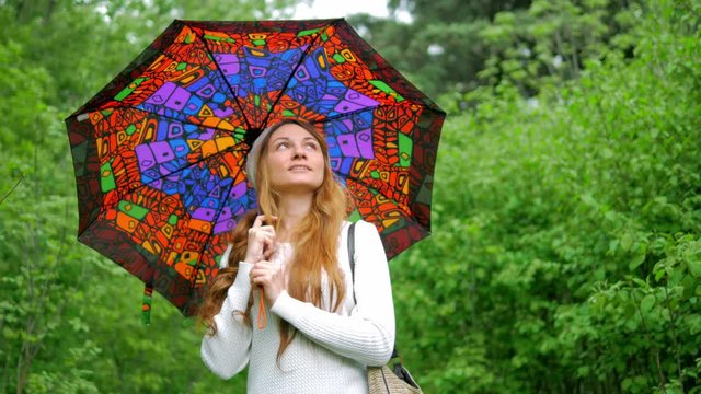 young girl walks in the park with an umbrella when it rains and looks up at the sky