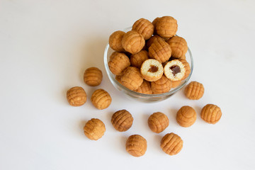 Round ruddy biscuit delicacy dessert in the form of small balls with boiled caramel inside. Cookies with filling are located in a transparent glass bowl and are scattered nearby on a white table.