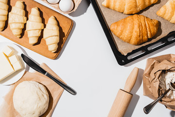 top view of raw and baked croissants on baking tray near ingredients on white background