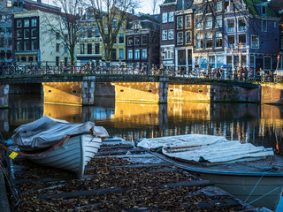 Fototapeta na wymiar Una barca junto a uno de los típicos canales de Amsterdam con la luz del atardecer pasando por un puente
