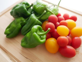 木製のトレイにたくさん盛られた新鮮なピーマンとプチトマト