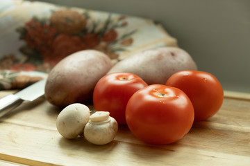  vegetables on a cutting board. Close-up of tomato, mushrooms and potatoes. And in the background is a knife.