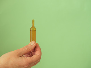 Hand with ampoule on green background wwith copy space