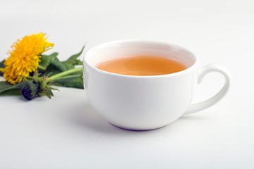Cup of purifying, diuretic tea of dandelion with fresh leaves and flowers on a white background. Fresh spring organic herbal, green drink. Copy space for text, selective focus