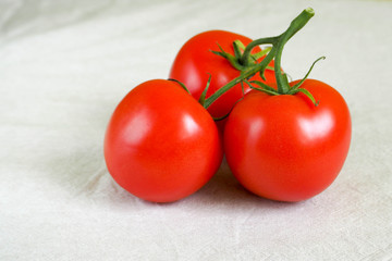 close-up of three red round tomatoes on a white linen surface. raw red vegetables