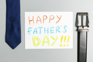 bright inscription "happy father's day" on a white sheet and a blue tie and black leather belt on a gray background.