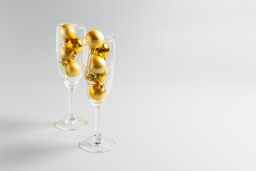  champagne glasses with golden christmas balls on gray background. New Year or Christmas party concept. copy space, minimalism