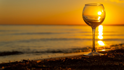 A glass on a sandy beach against the background of the sunset.
