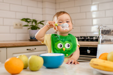 Happy child girl in the kitchen eats a delicious cottage cheese and porridge.