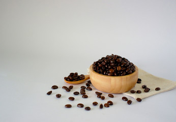 Fototapeta na wymiar Roasted coffee beans in a wooden cup and spoon placed on a calico, translucent background.