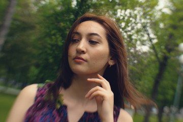 Naklejka premium Portrait of a girl in a park. Face of a beautiful asian girl close-up. She looks down and holds her hand near the chin.