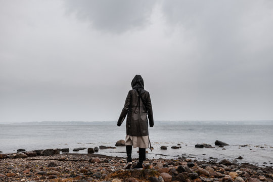 Young Women in rainjacket standing at coastline in rainy weather and clouds