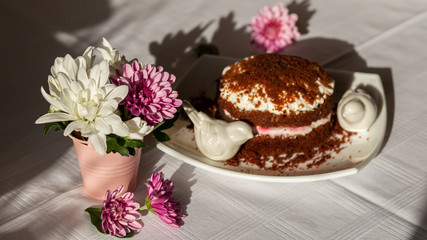 Freshly baked homemade chocolate cake with cream cheese on white plate. Chrysanthemums on the table.