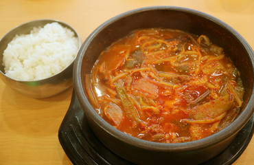 Pot of Kimchi Jjigae or Korean Hot and Spicy Kimchi Stew Served with a Bowl of Rice on Wooden Table