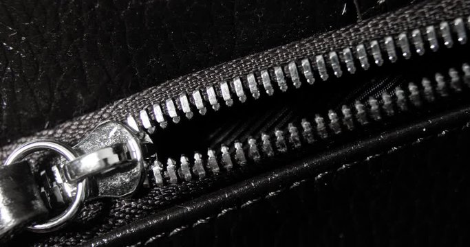 Man zips and unzips metal zip a leather black bag, hand closeup view. Macro shot of unzipping and zipping metallic zipper on black leather accessory with guy's hand.