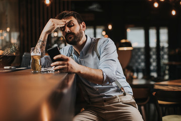 Man drinking beer, smoking cigarette and using mobile phone at pub