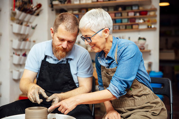 Senior woman spinning clay on a wheel with teacher at pottery class