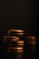 
A column of four delicious brown chocolate chip cookies. Two other cookies in the back area. Dark background.