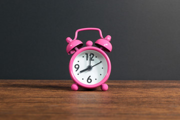 
pink alarm clock on wood, a black background