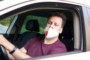 A man driving a car in a medical respirator during coronavirus outbreak, a taxi driver in a mask, protection from the virus. Driver in white car. Quarantine, covid-19.