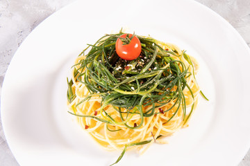 Spaghetti with agretti, a spring vegetable from Italy, on a white plate on a gray background