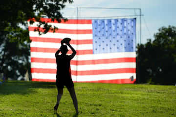 The Silhouette of a football player hands the ball in front of huge United States National Flag erected in National Gardens Park in Washington DC during Memorial weekend