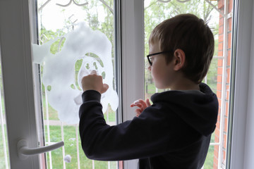 the boy draws on the window with foam for Windows, the child helps his mother to clean the house, the boy assistant washes the window with detergents