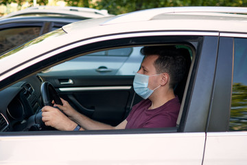 Fototapeta na wymiar A man driving a car in a medical face mask during coronavirus outbreak, a taxi driver in a mask, protection from the virus. Quarantine, covid-19.