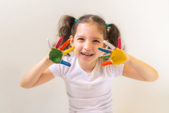 Happy little girl with painted palms on a light background