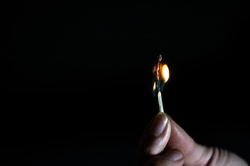 Female hand holding a burning wooden match. Black background. Bright warm fire. One match. Fire of hope. Orange yellow flame and warmth. Darkness around. Wood texture. Highly flammable, blue-orange 