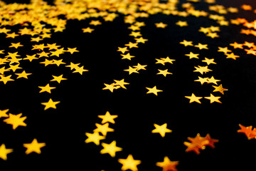 Golden stars confetti scattered on a black background. Creative holiday concept.