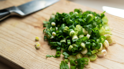 Handful of finely chopped fresh green onions and kitchen knife on wooden board, rustic wooden table. Closeup cooking vegetables in kitchen. Ingredients for Thai foods.