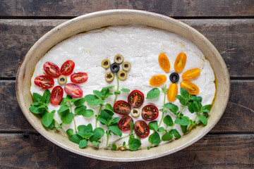 Obraz na płótnie Canvas Homemade dough for delicious, italian focaccia in round baking bowl. Decoration is made of cherry tomatoes, olives and fresh herbs.