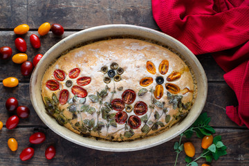 Homemade, beautiful and delicious, italian focaccia in round baking bowl. Decoration that looks like flowers in garden is made of cherry tomatoes, olives and fresh herbs.