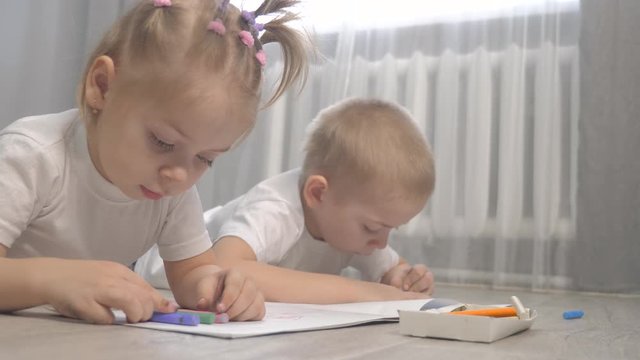 happy family brother and sister teamwork concept. little boy and girl draw on floor in a sketchbook. brother and sister in the room draw with crayons lifestyle