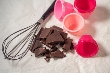 Getting ready for baking chocolate cupcakes, pink silicone forms and whisk with broken dark chocolate pieces on a baking paper