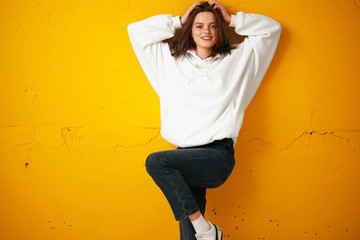 Portrait of a young pretty female student in a white hoodie, casual clothing against a concrete...