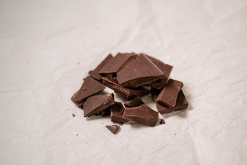 Broken dark chocolate bar on a white baking paper, sweet treat