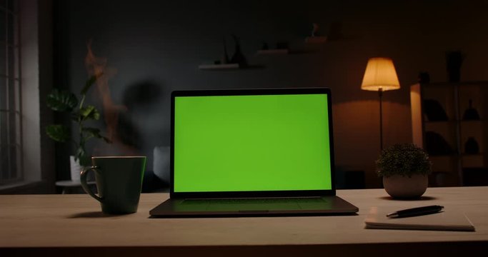Chroma key green screen template - a laptop computer on a desk in cozy living room at night. Computer set for distance learning and remote work, technology concept 4k footage