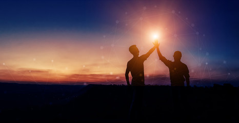 Two silhouette man colliding hand, showing success on the top of the hill in twilight, concept...