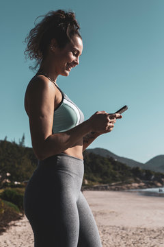 Young attractive woman smiling chatting on smartphone at the beach on sunny day with blue sky.